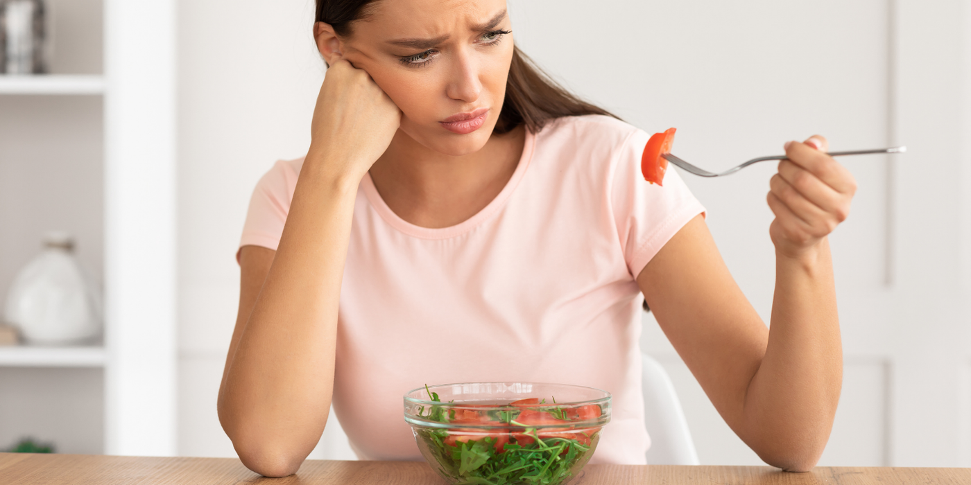 Frau schaut lustlos auf Salatschüssel