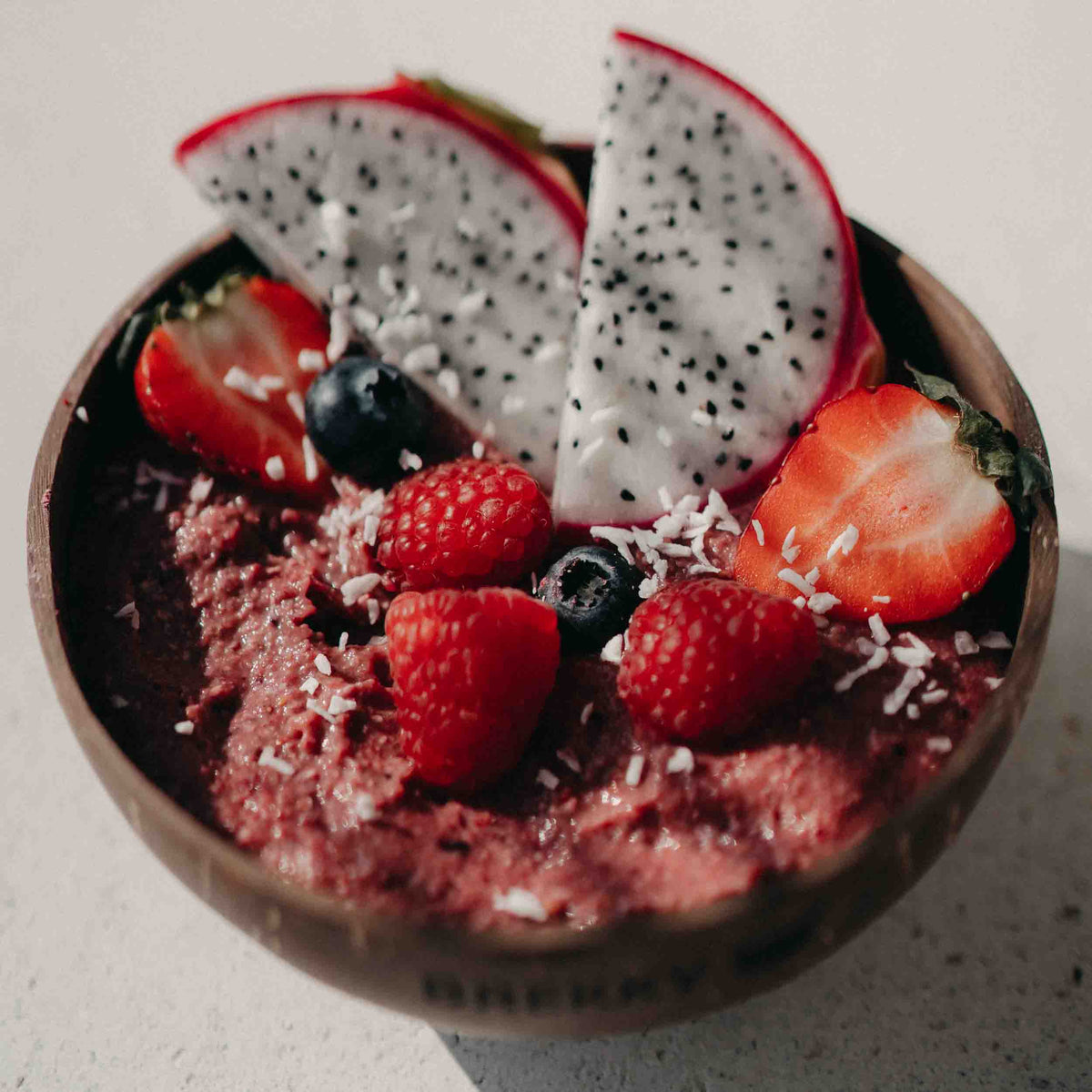Smoothie Bowl mit Drachenfrucht und Beeren in Kokosschale