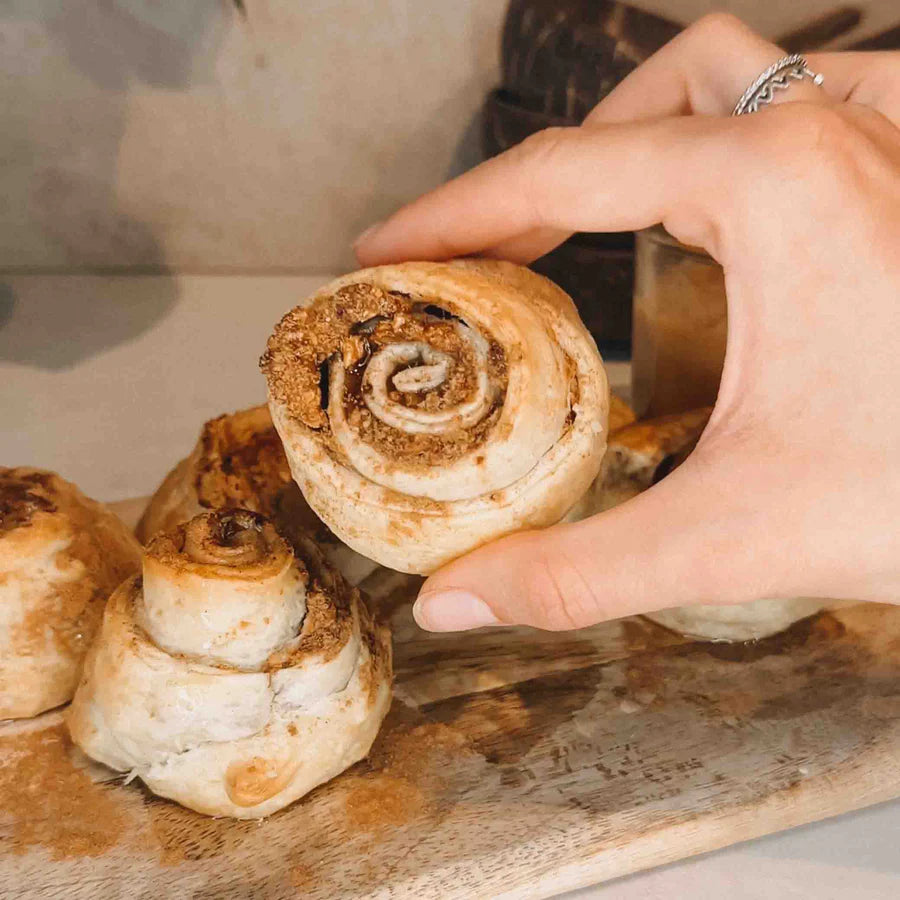 Hand greift nach Zimtschnecke auf Holzbrett