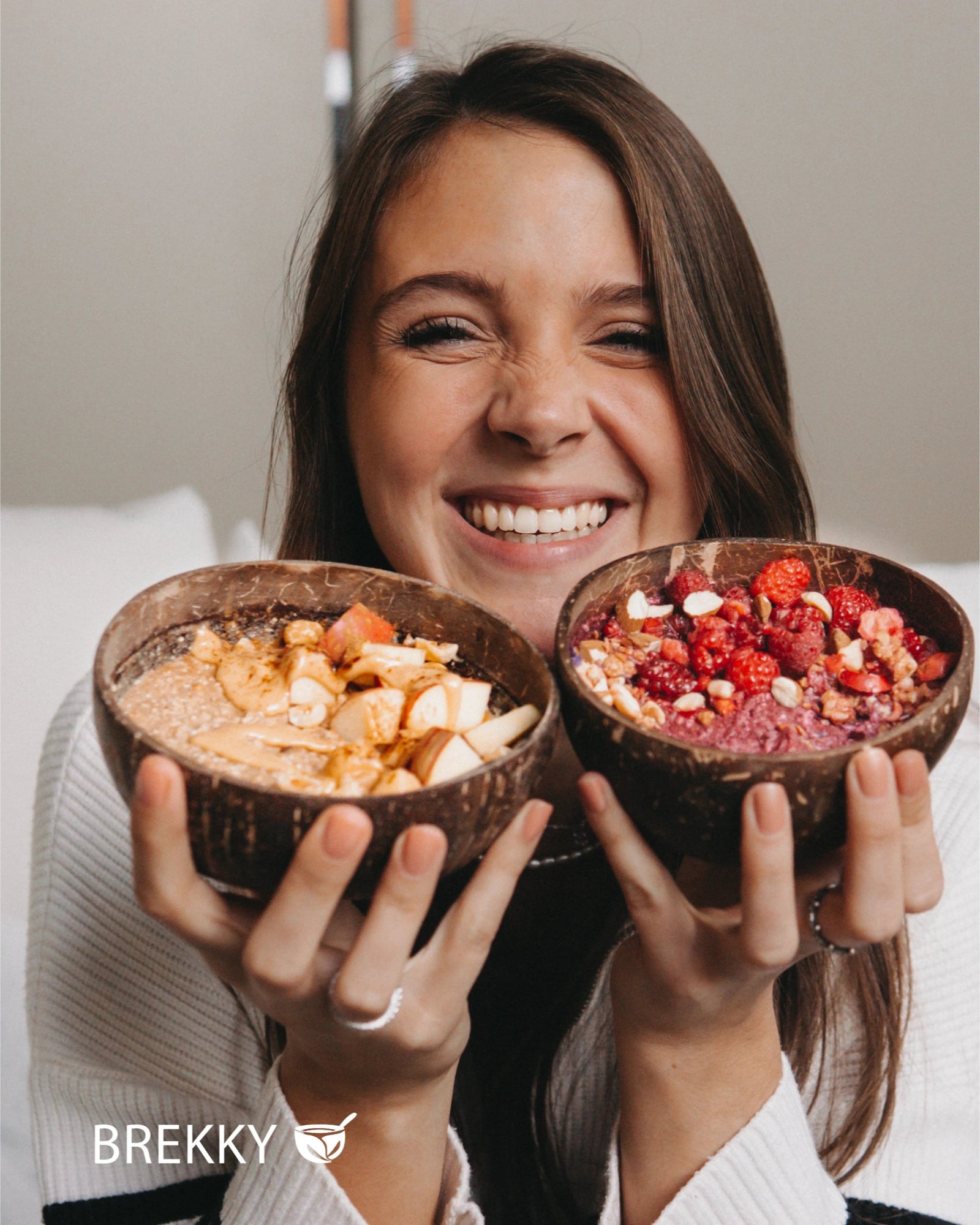 Lachende Frau hält zwei Smoothie Bowls in Kokosschalen